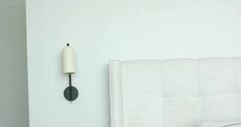 Minimalist bedroom corner showing tufted upholstered headboard and soft cream wall sconce