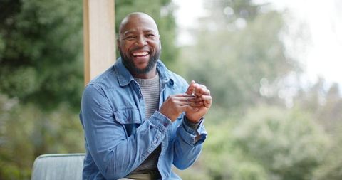 Smiling African American Man Sitting on Porch Holding Smartphone Enjoying Relaxed Outdoor Moment