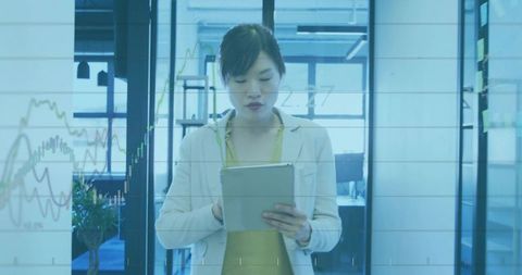 Businesswoman Holding Tablet and Analyzing Financial Graphs on Glass Wall in Modern Office