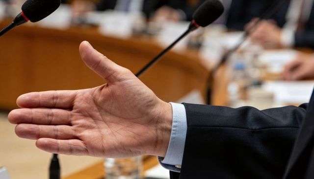 Hand extending for handshake during boardroom meeting with microphones and suit cuff