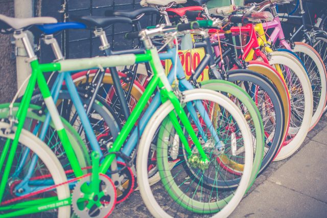 Series of brightly colored bicycles lined up along a city street, creating a vibrant and lively atmosphere. Perfect for use in articles about urban transport, bicycle culture, sustainable travel, bike-sharing programs, or city living.