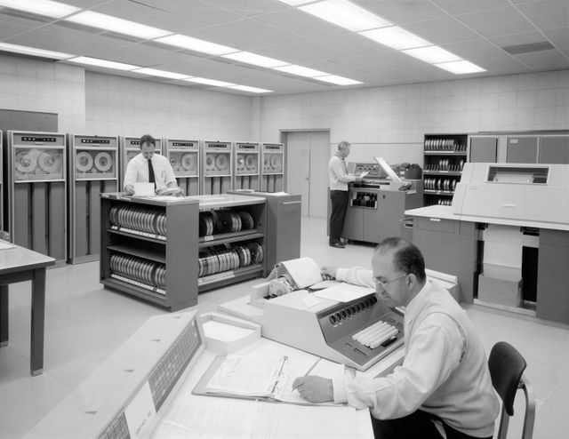 This scene shows three engineers working on the Honeywell H-800 data processing system in a research facility, accentuating the scale and visual complexity of early computing. This image is ideal for illustrating the history of technology, the evolution of computer systems, and vintage research environments. It is suitable for educational content, articles about computing history, or decor for tech firms and museums showcasing computing heritage.