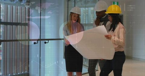Architects reviewing blueprint in modern atrium wearing hard hats, planning construction
