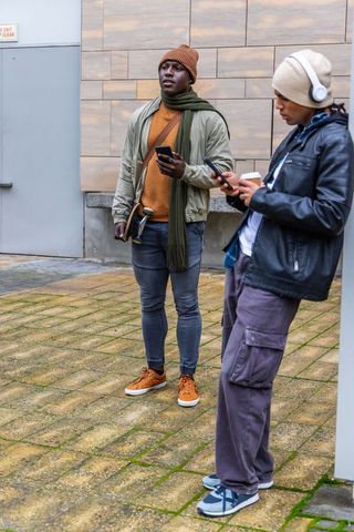 Diverse friends checking smartphones with skateboard and coffee in urban winter style
