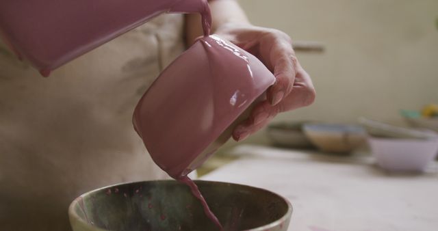 Close up view of female potter pouring paint from a jug on pot at pottery studio. hygiene and social distancing in the pottery studio during coronavirus covid 19 pandemic.