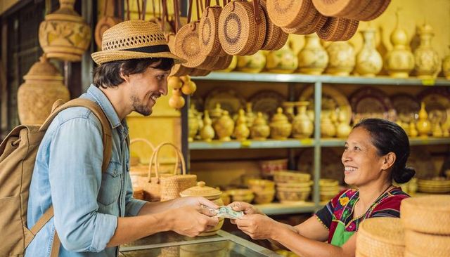 Traveler handing cash to artisan vendor in colorful market selling wicker baskets, pottery