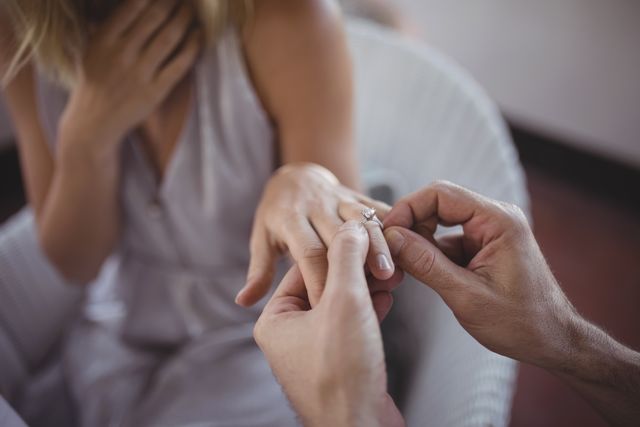 Man placing engagement ring on woman's finger, capturing a romantic and intimate moment. Ideal for use in wedding planning, relationship advice, romantic greeting cards, and jewelry advertisements.