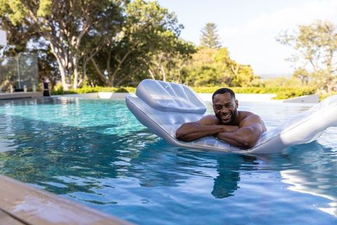 Mature african american man relaxing on inflatable pool lounger by luxury backyard pool