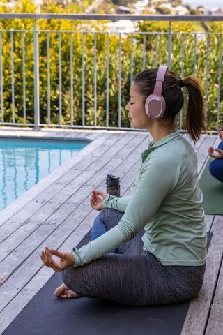 Woman meditating with headphones on poolside deck practicing yoga and mindfulness