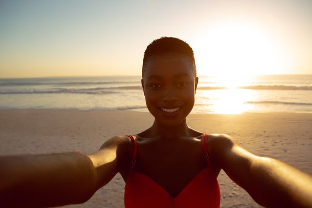 Woman taking a selfie on the beach during sunset. Ideal for use in travel blogs, vacation advertisements, lifestyle magazines, and social media campaigns promoting beach destinations and outdoor activities.