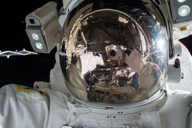 Image shows astronaut during spacewalk with reflection visible on helmet visor. Suitable for illustrating topics related to space exploration, astronautics, NASA missions, technical advancements in space travel, the International Space Station, and the wonders of outer space.