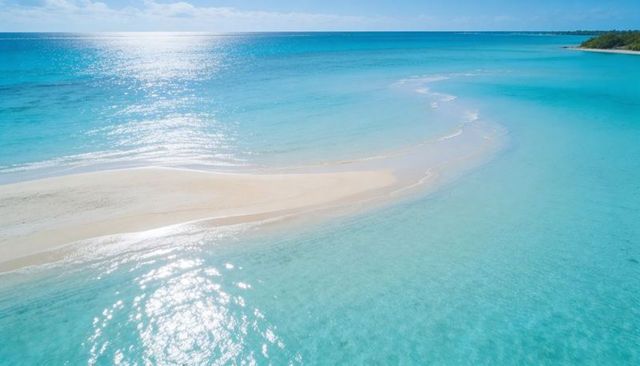 Glinting turquoise lagoon with curving white sandbar and distant treeline