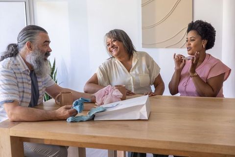 Diverse multigenerational family sharing gifts, laughing and chatting around wooden table