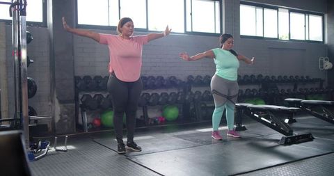 Two diverse women exercising with resistance bands in gym workout for strength and positivity