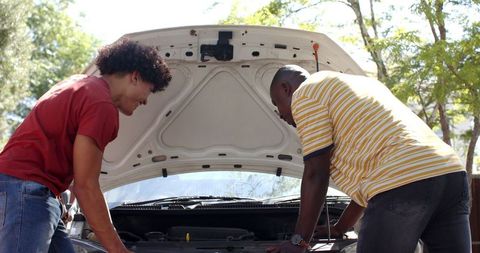 Friends conducting car inspection outdoors on sunny day