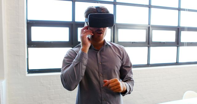 Man Using Virtual Reality Headset While Talking on Smartphone in Modern Office - Download Free Stock Images Pikwizard.com