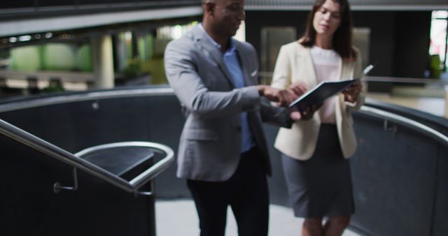 Two business professionals standing and discussing work on a digital tablet in a modern office environment. Ideal for depicting business communication, teamwork, corporate meetings, technology use in the workplace, and professional collaboration.