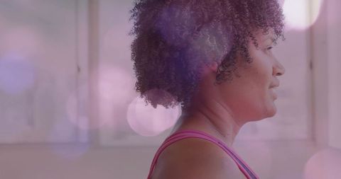 Serene woman standing in pastel studio wearing pink tank top with calm soft bokeh light