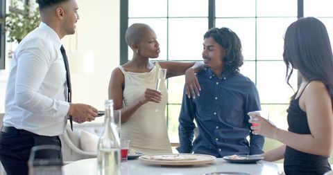 African american woman leaning on friend mingling at kitchen island holding champagne