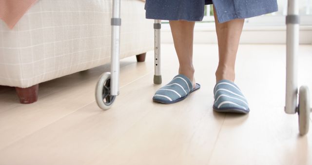 Person wearing striped slippers using a walker indoors, emphasizing mobility and independence of elderly individuals. Ideal for use in healthcare, senior care promotions, home safety tips, and aging-related articles.