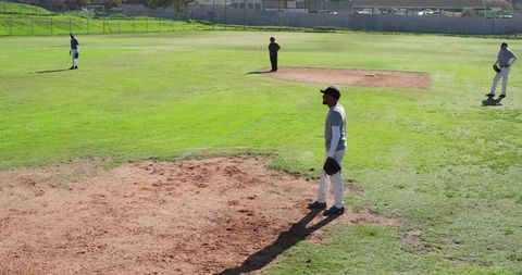 Sunlit diverse baseball team standing on infield holding gloves and waiting at practice
