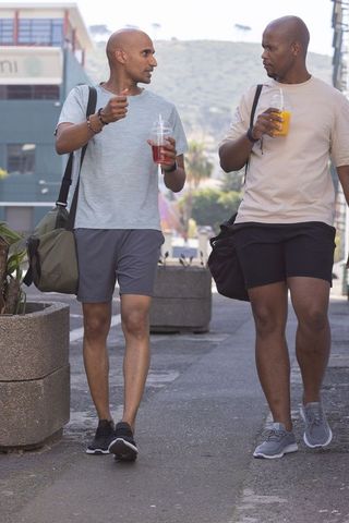 Two african american men walking together sipping refreshing juices carrying duffel bags