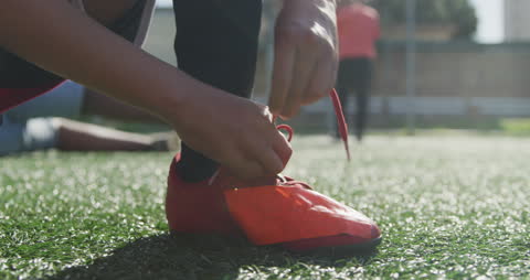Young Soccer Player Tying Red Cleats on Sunny Field