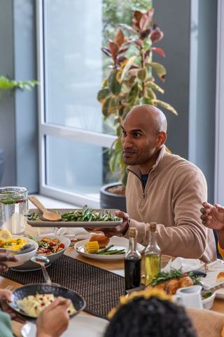Indian man serving green beans at casual family dinner around communal dining table
