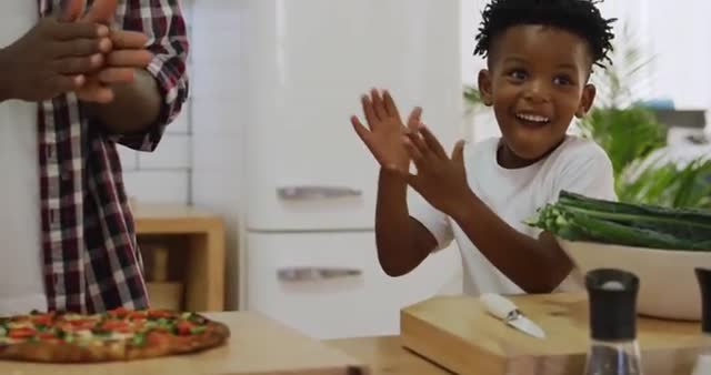 Father and young son joyously clapping and giving high fives in a home kitchen while cooking. Warm and loving family interaction highlighting father-son bond. Ideal for use in family-oriented advertising, parenting blogs, and articles promoting family activities and cooking at home.