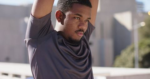 African American man stretching arms overhead on urban rooftop warming up for workout