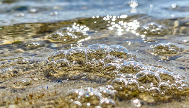 Glassy bubbles clinging to wet sand with sunlit reflections and iridescent sparkle