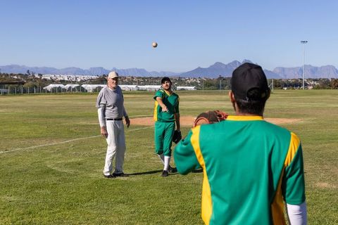 Baseball coaching drill with coach mentoring players throwing and catching on sunny outfield
