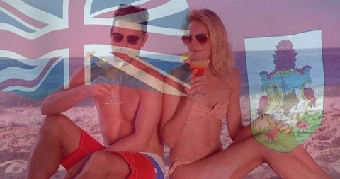 Couple relaxing on bermuda beach sipping cocktails with flag overlay summer vacation