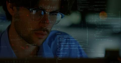 Software developer coding late at dim workstation with code reflecting on glasses