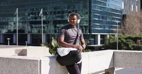 Young African American man leaning on railing wearing white headphones in urban plaza