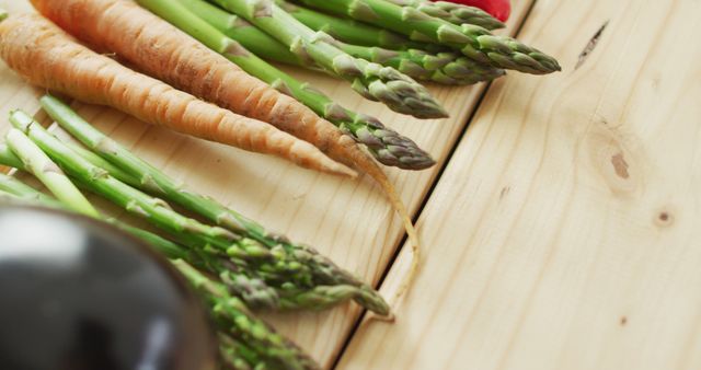 Fresh asparagus and carrots are arranged on wooden table. Great for ads, blogs or articles about healthy eating, organic produce, or cooking. Ideal for recipes, food blogs, or diet plans.