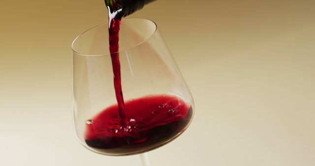 Close-up view of red wine being poured into a glass on a neutral beige background. The image can be used for wine advertisements, restaurant menus, celebration invitations, or articles on wine culture and tasting.