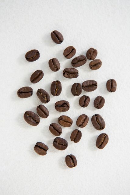 Roasted coffee beans scattered on a white background, suitable for use in food and beverage websites, promotions for coffee brands, or cafe decor. Ideal for illustrating articles related to coffee brewing, caffeine, or coffee-related recipes.
