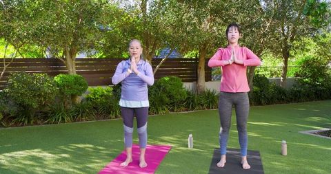 Asian mother and daughter practicing yoga outdoors in morning sun