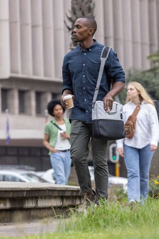 Black professional walking with coffee and messenger bag through urban office plaza