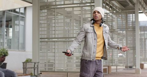 Young man standing in urban plaza holding smartphone, gesturing while talking