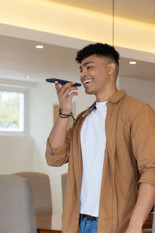 African American man speaking into smartphone in modern dining room, using voice assistant