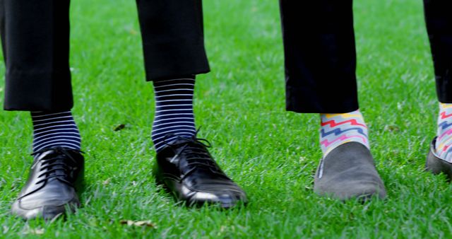 Two men with different colorful socks standing on green grass wearing dress shoes and loafers. Great for themes related to fun, fashion, footwear, outdoor activities, and personality expression.