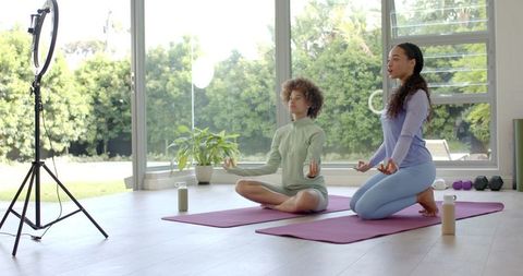 African American women practicing seated yoga and guided meditation in garden-view studio