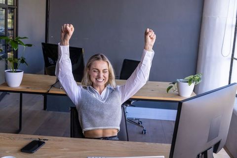Joyful Woman Celebrating Success at Modern Office Desk