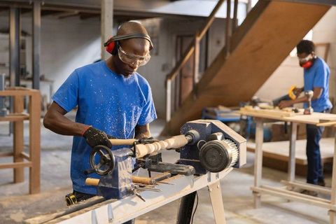 African american woodworkers operating lathe and measuring timber in carpentry workshop