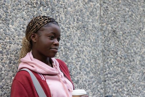 African-american woman leaning on pebble wall holding coffee cup, casual urban portrait