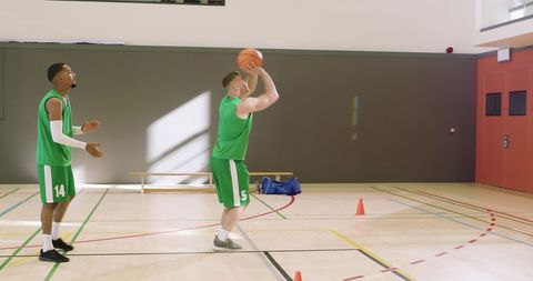 Basketball players practicing shooting drill with cones in indoor gym teamwork training
