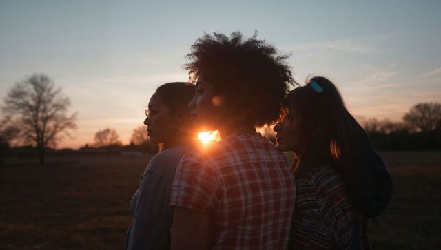 Three friends watching sunset in open field backlit silhouette golden hour sun flare