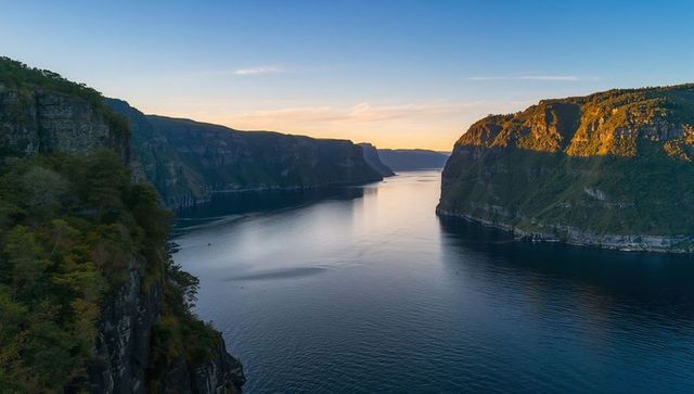 Golden hour fjord canyon with narrow channel and small boat, aerial coastal panorama